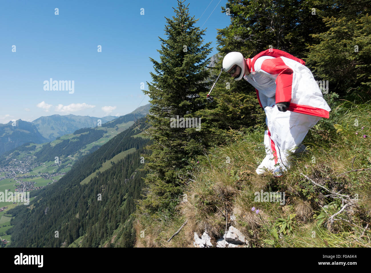 Wingsuit BASE jumper is getting ready to jump off a cliff and checking the altitude by facing downward & adjusting his wings. Stock Photo