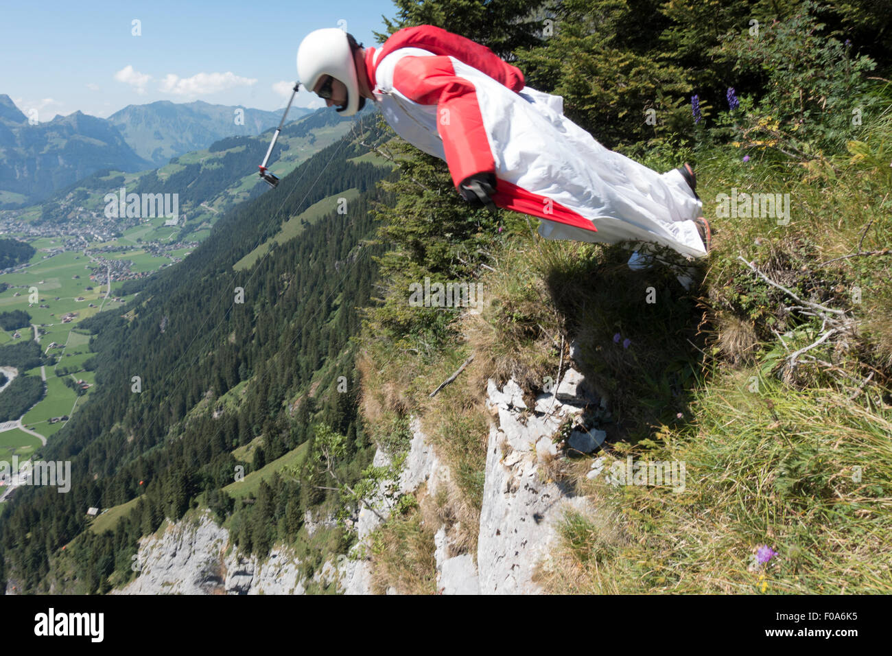 Wingsuit BASE jumper is exiting off a cliff downwards the valley and starts flying with his birdman suit. Stock Photo