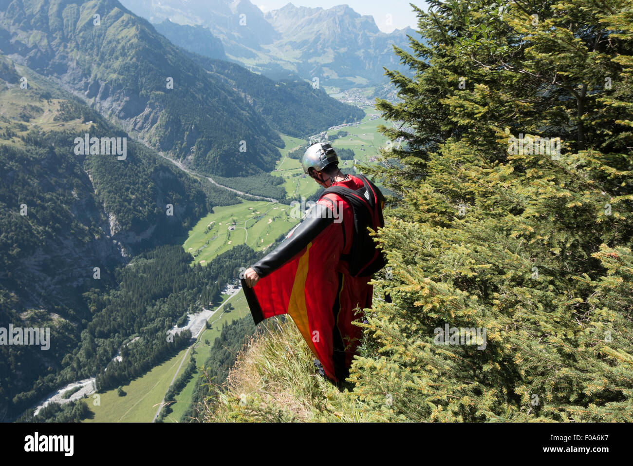 Wingsuit BASE jumper is getting ready to jump off a cliff and checking the altitude by facing downward & adjusting his wings. Stock Photo