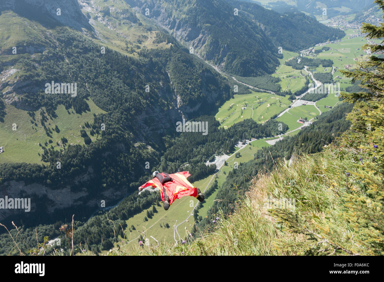 Wingsuit BASE jumper is flying down from a grass-cliff into the valley with his birdman suit. Stock Photo