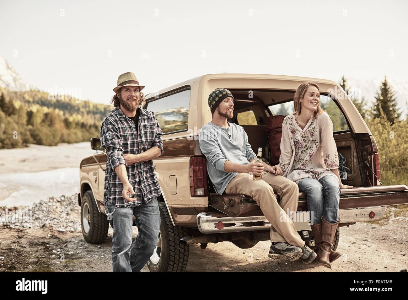 Three people sitting on back of pickup truck smiling Stock Photo