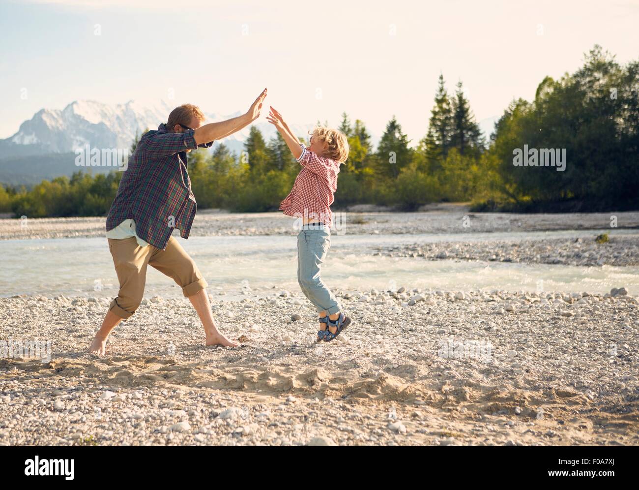 Side view of young man and boy jumping, doing high five, Wallgau, Bavaria, Germany Stock Photo