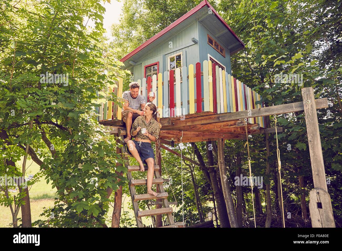 Young couple sitting on ladder of tree house Stock Photo