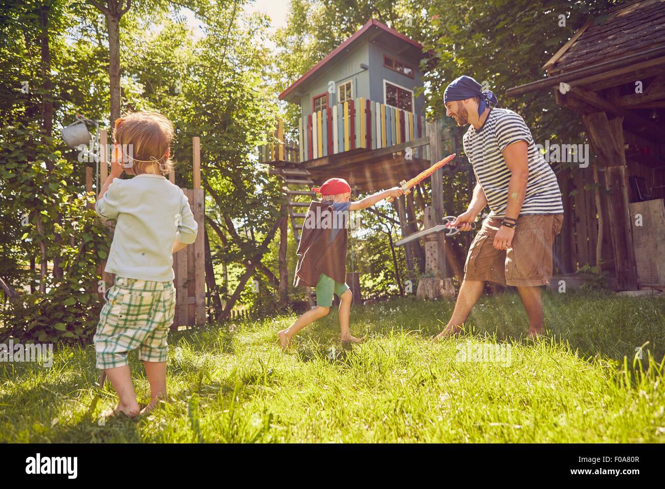 Father and two sons in garden, wearing costumes, playing with pretend
