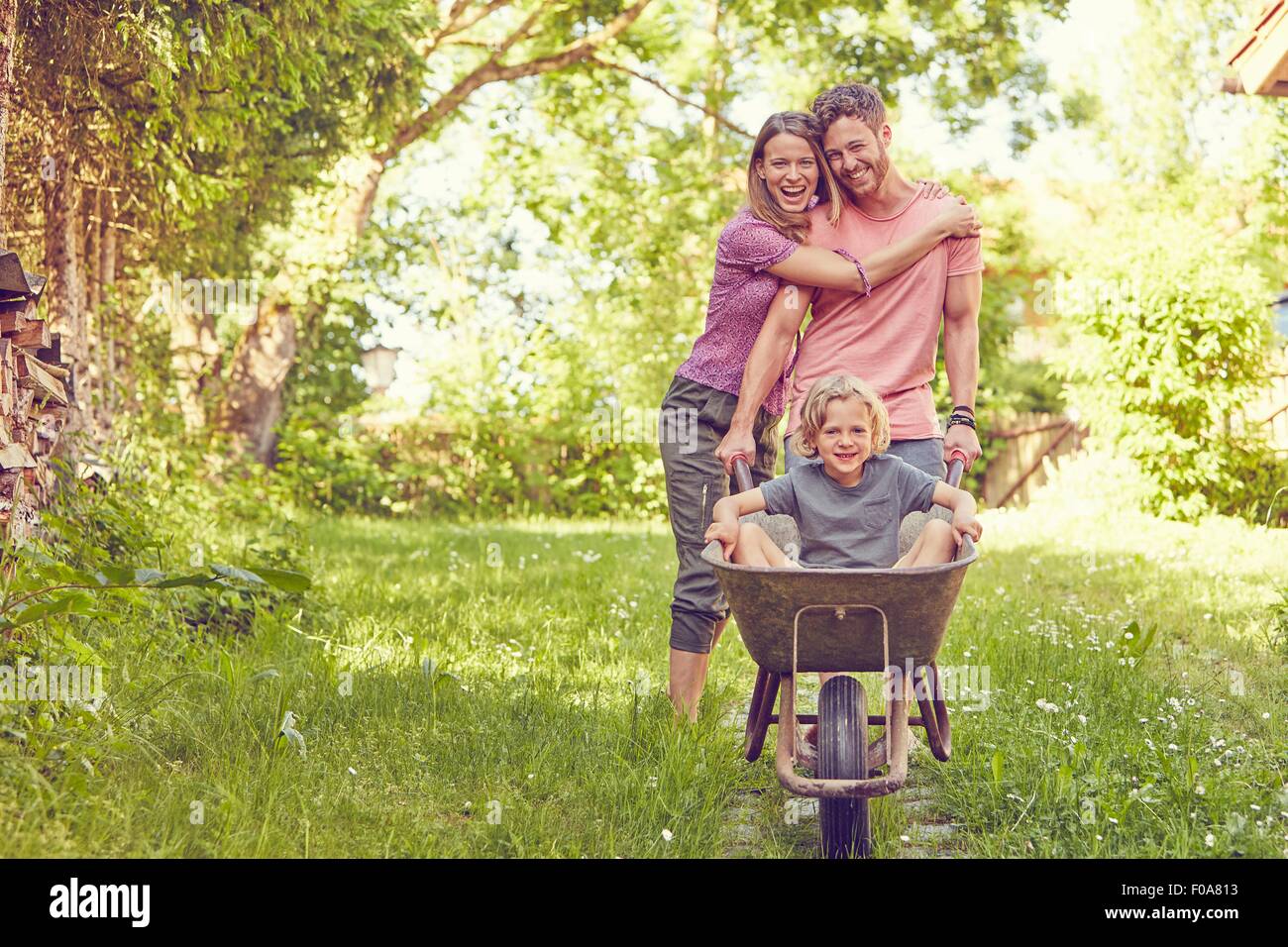 Portrait of young family, father pushing son in wheelbarrow Stock Photo