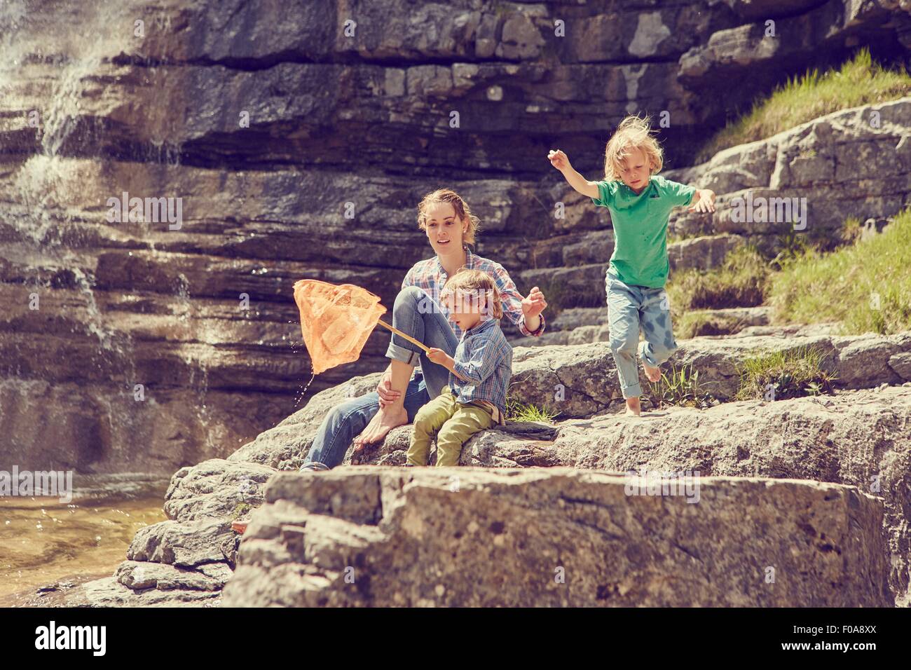 Mother and sons, sitting on rocks by waterfall, fishing with net Stock Photo