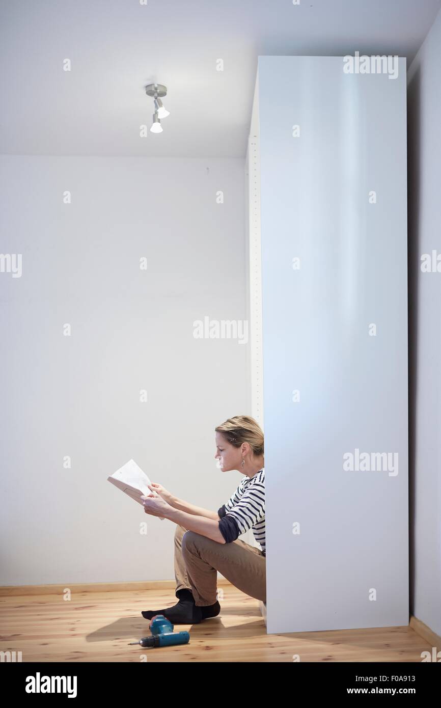 Mature woman sitting reading instruction manual for flatpack closet Stock Photo