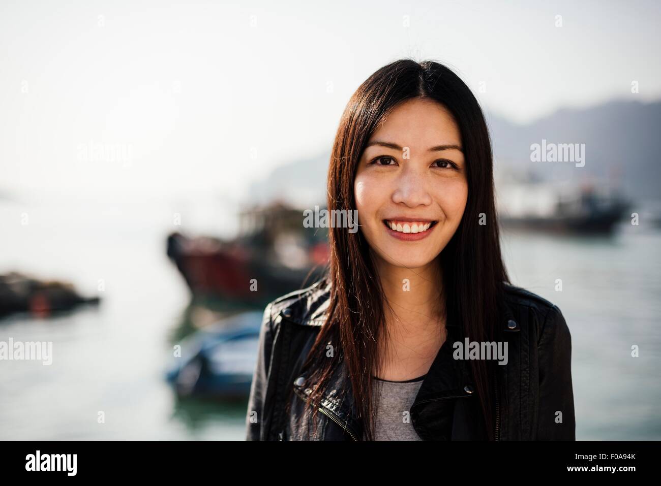 Portrait of young woman in front of boats on water, looking at camera smiling Stock Photo