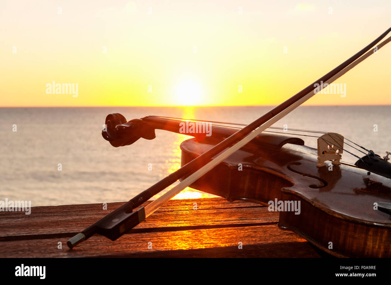 Sunset over sea with violin and bow on bench Stock Photo