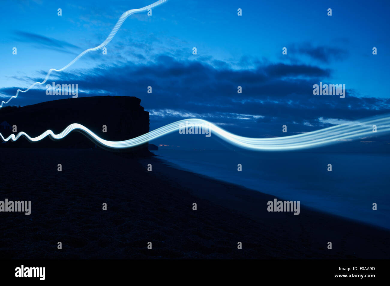 Wavy line light trails on silhouetted beach at night Stock Photo