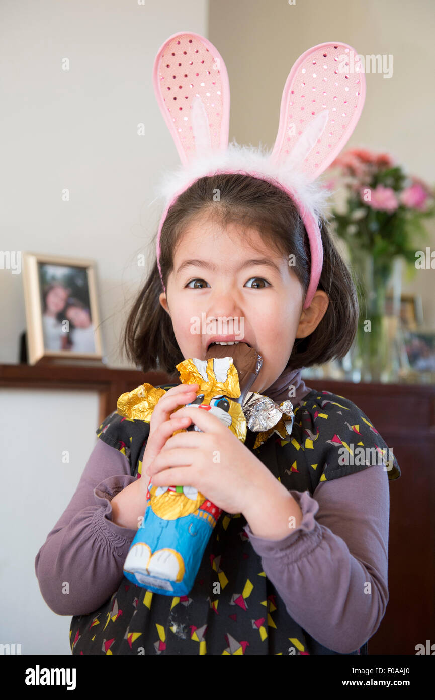 Young girl wearing bunny ears, just about to bite into chocolate bunny