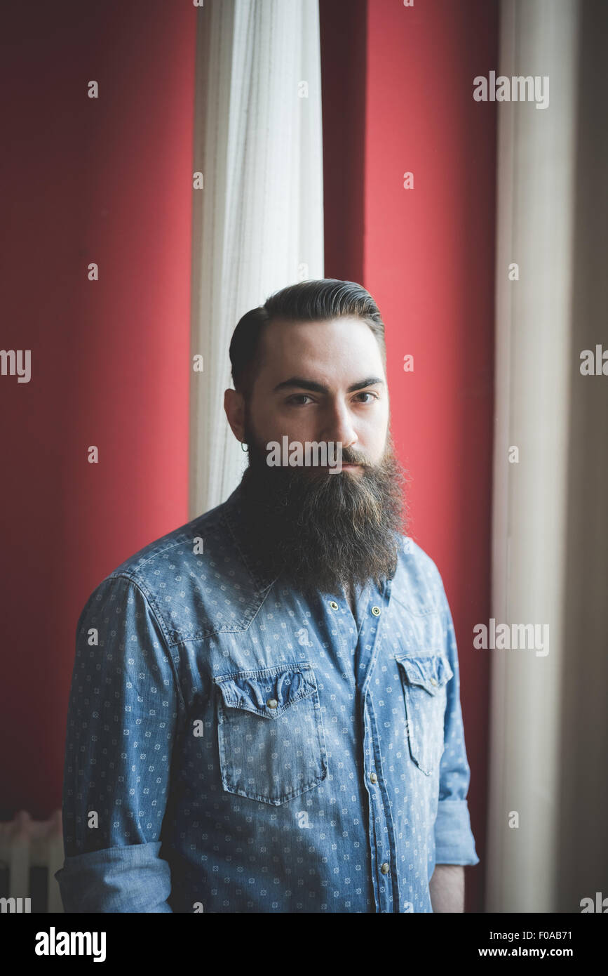 Young bearded man standing by window Stock Photo