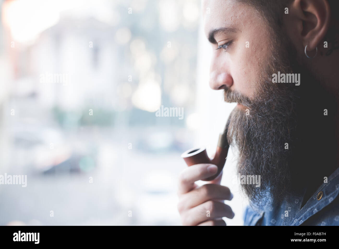 Young bearded man smoking pipe by window Stock Photo