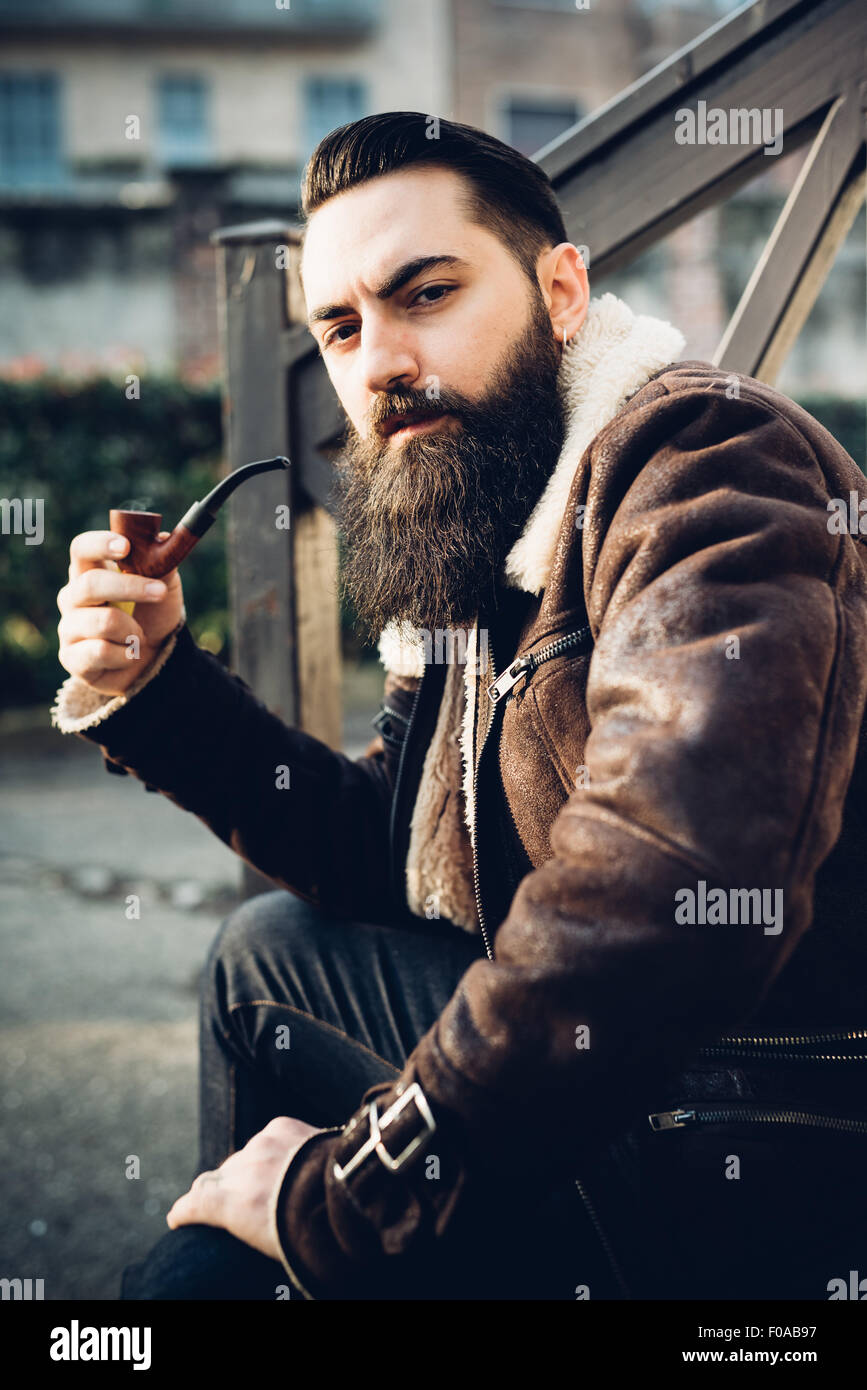 Young bearded man smoking pipe on steps Stock Photo