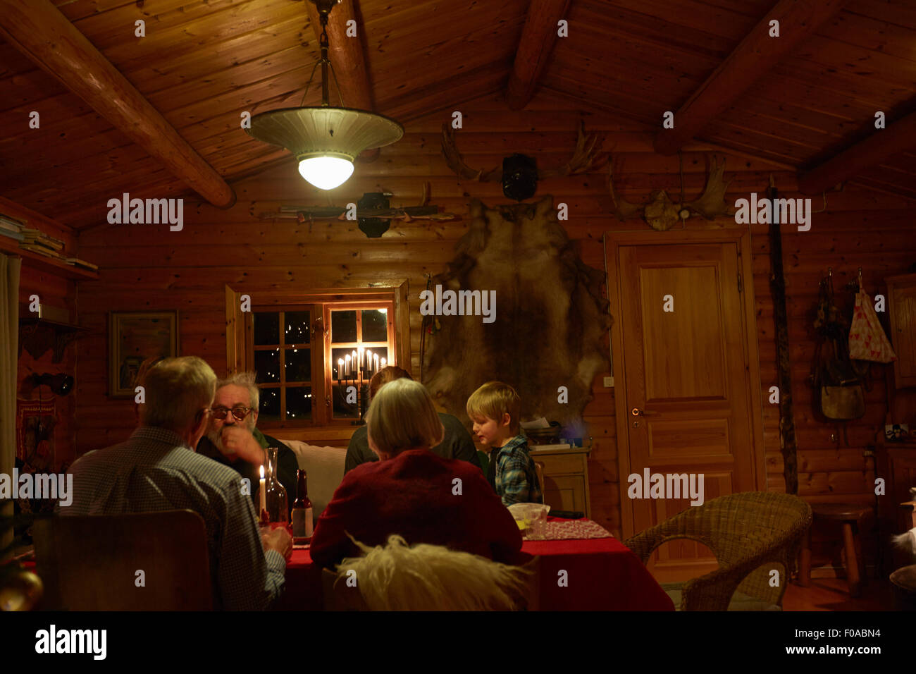 Three generation family sitting talking at Christmas table in log cabin at night Stock Photo
