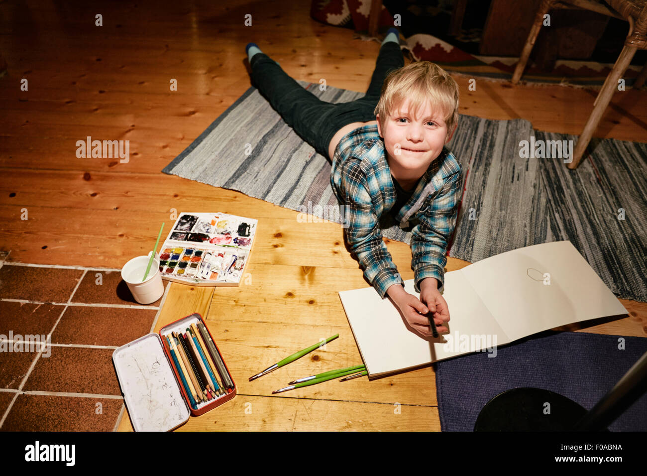 Boy lying on floor with watercolor paints and sketch pad Stock Photo