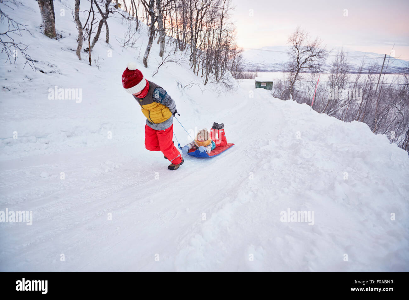 Boy pulling brother on toboggan up snow covered hill, Hemavan,Sweden Stock Photo
