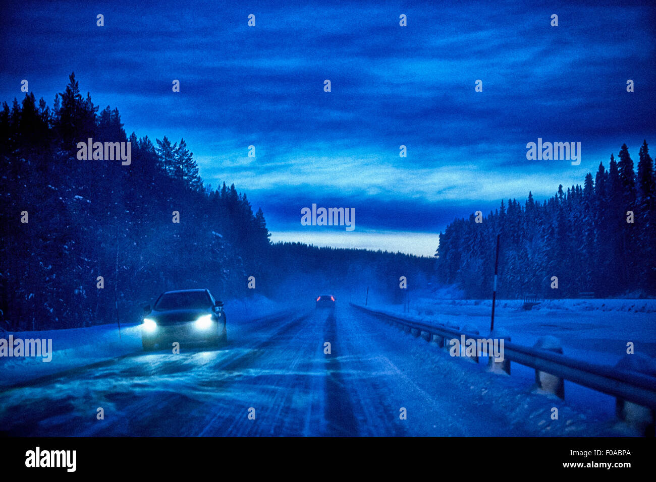 Car headlights on snow covered highway at dusk, Hemavan, Sweden Stock Photo