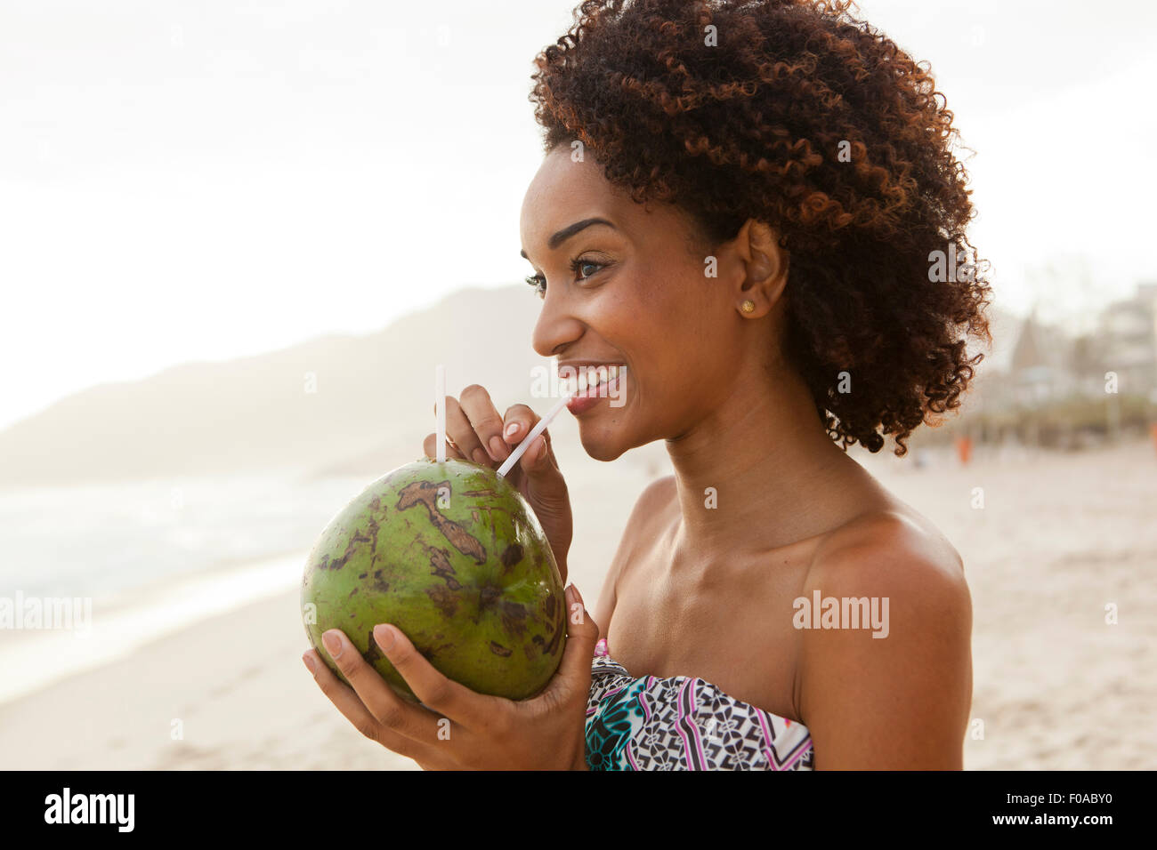 Portrait of young woman drinking coconut milk on beach, Rio De Janeiro, Brazil Stock Photo