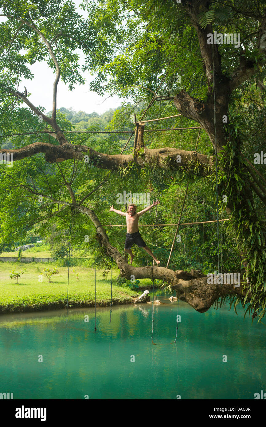 Mature man jumping mid air into turquoise lagoon, Vang Vieng, Laos Stock Photo