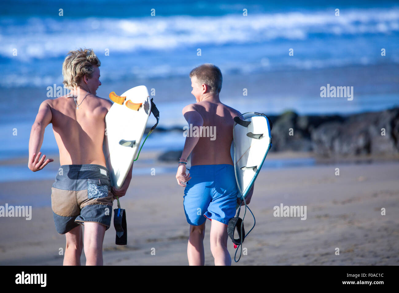Two teenage male surfers running toward sea, Fuerteventura, Spain Stock Photo