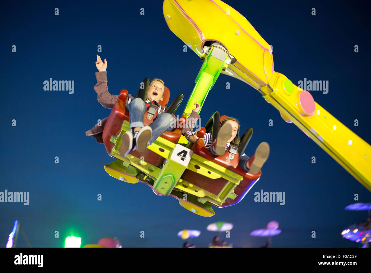 Brother and sister mid air on fairground ride at night Stock Photo