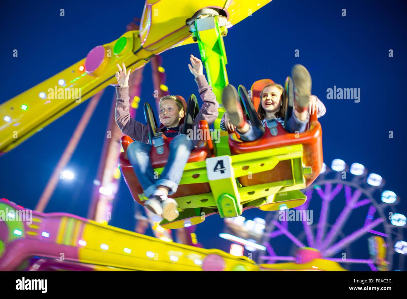 Sister and brother mid air on fairground ride at night Stock Photo