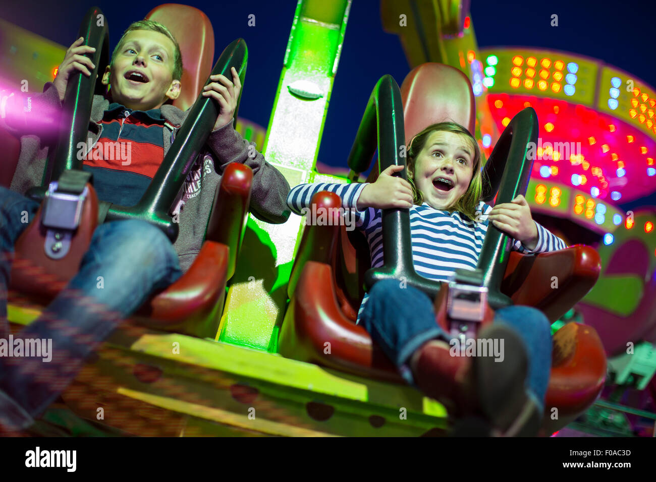 Sister and brother on fairground ride at night Stock Photo