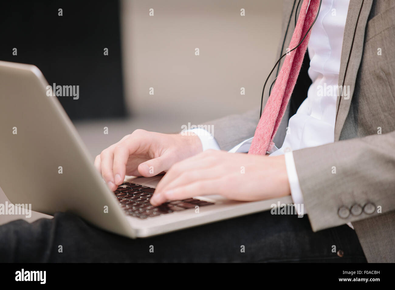 Cropped shot of young city businessman sitting on sidewalk typing on laptop Stock Photo