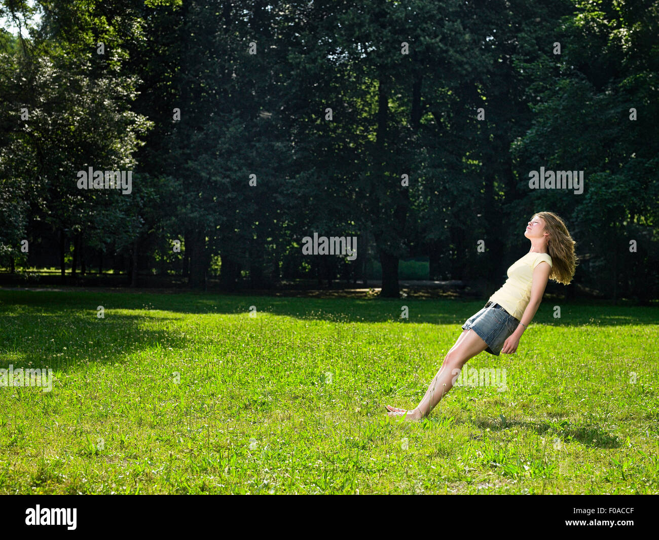 Young woman in park free falling backwards with eyes closed Stock Photo