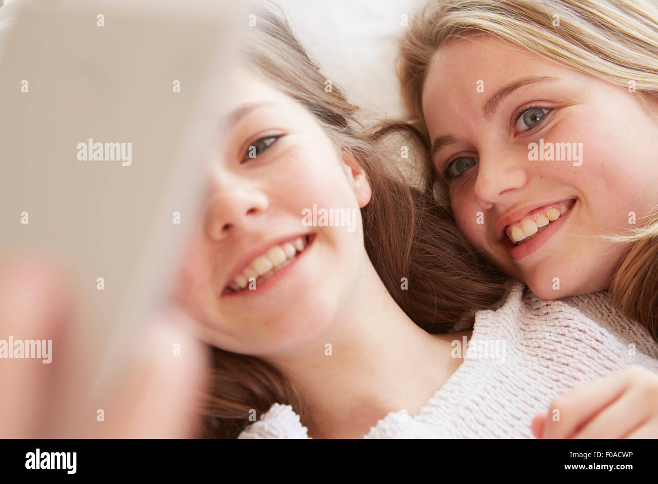 Close up of two girls lying on bed taking smartphone selfie Stock Photo