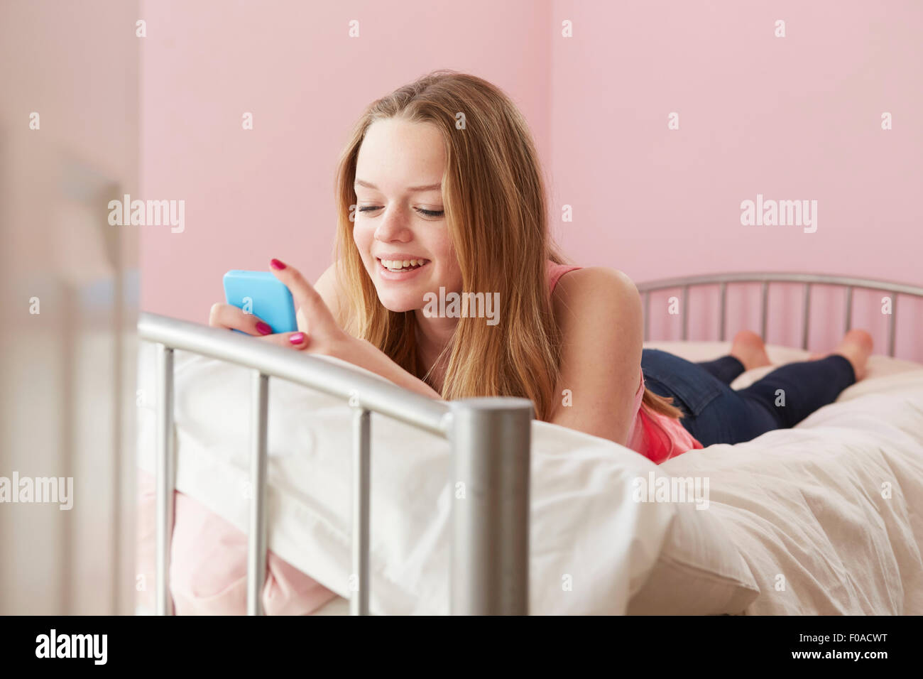 Girl lying on bed reading text message on smartphone Stock Photo