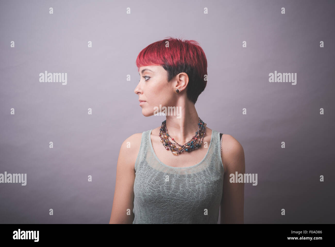 Studio portrait of young woman with short pink hair looking over her shoulder Stock Photo