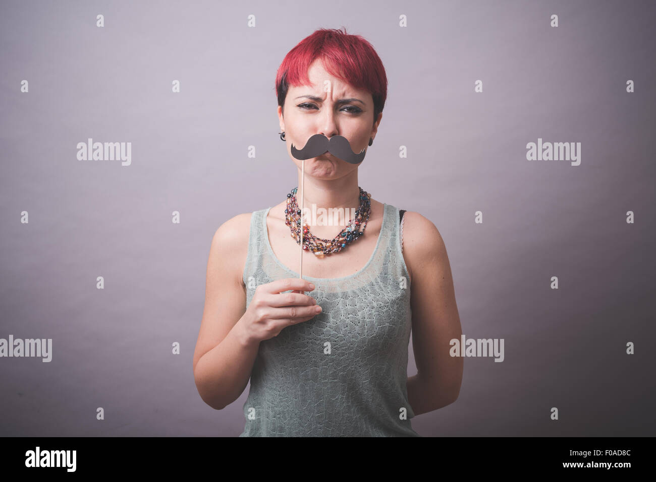 Studio portrait of confused young woman holding up mustache in front of face Stock Photo