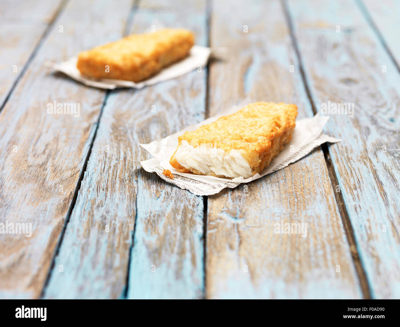 Two fried chunky battered haddock pieces on wooden table Stock Photo