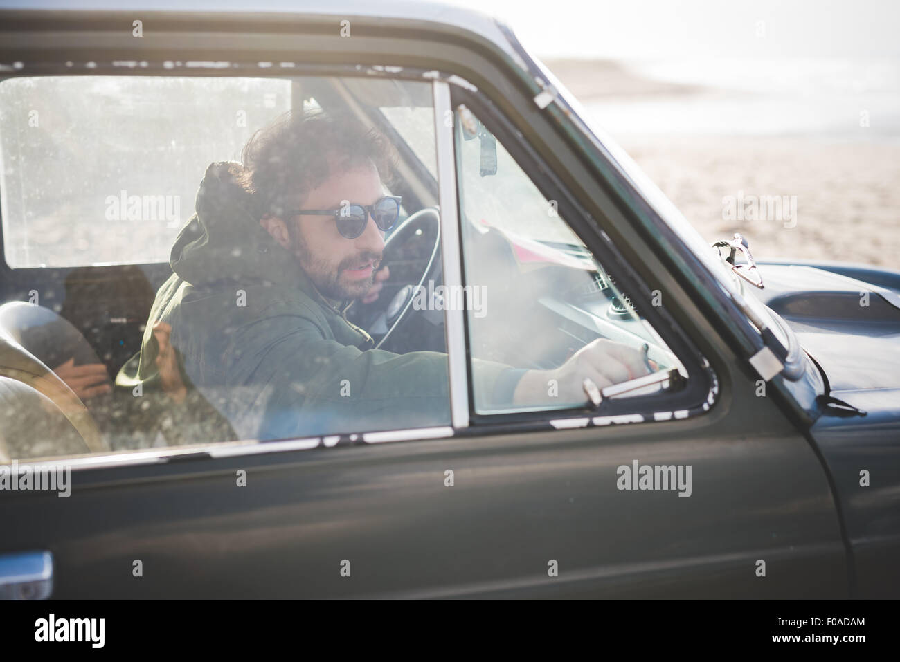 Man in parked vintage car lat beach fastening window Stock Photo
