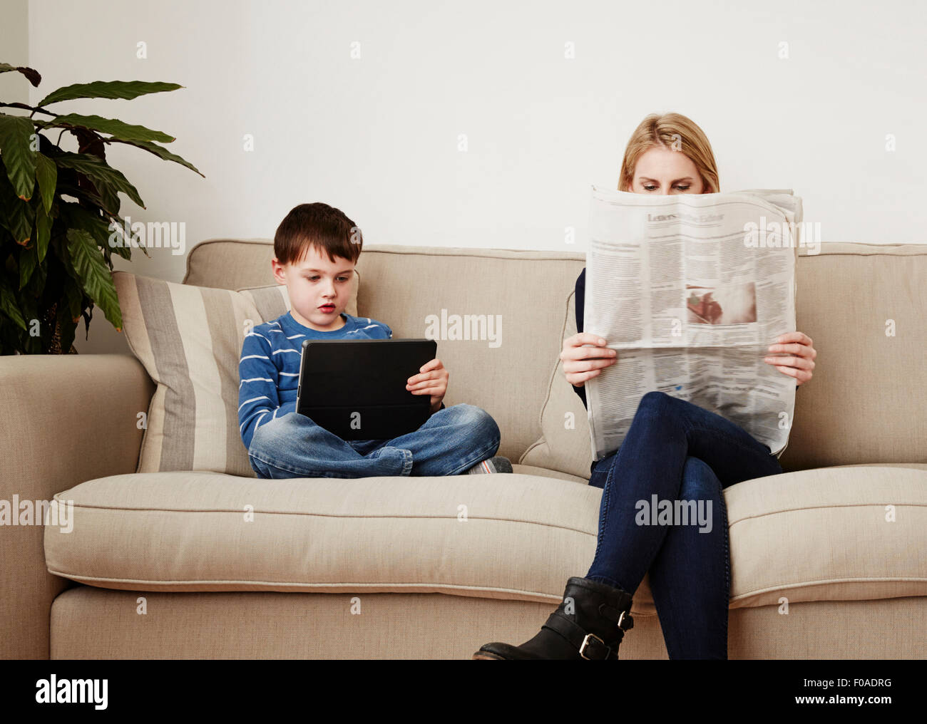 Young boy using digital tablet, mother reading newspaper Stock Photo
