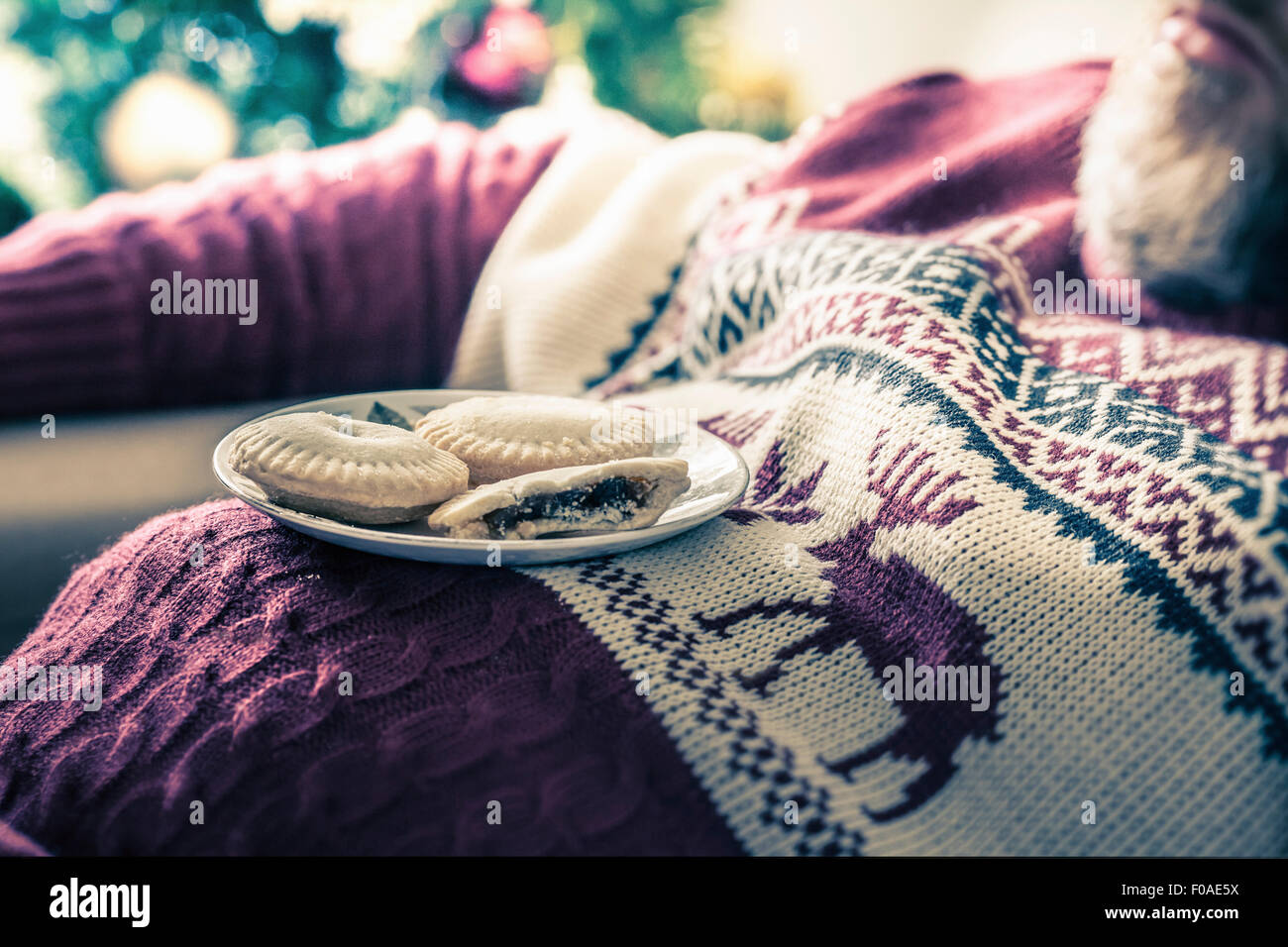Man wearing sweater asleep with mince pies on chest Stock Photo