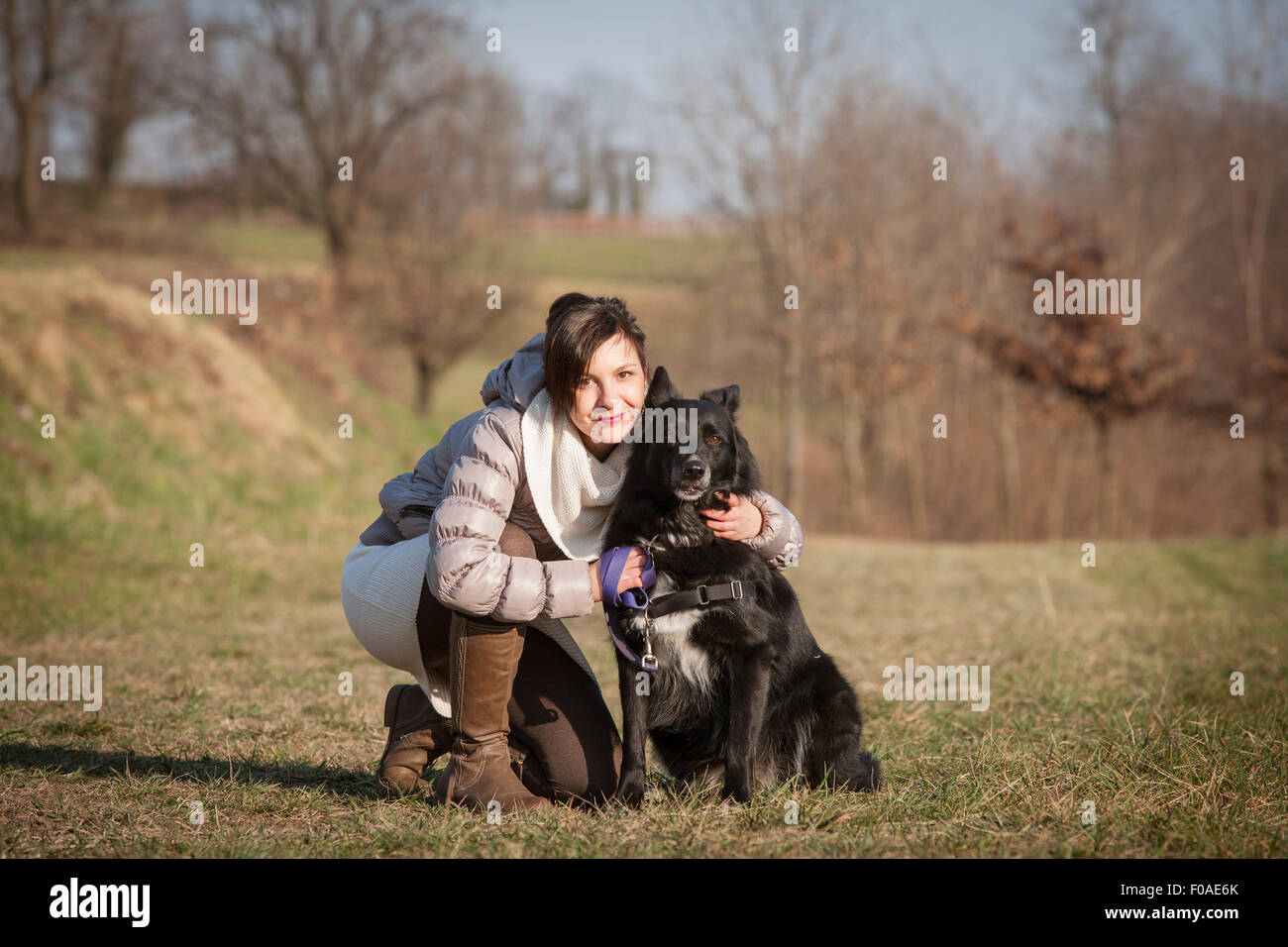 Portrait of mid adult woman kneeling with her dog in field Stock Photo
