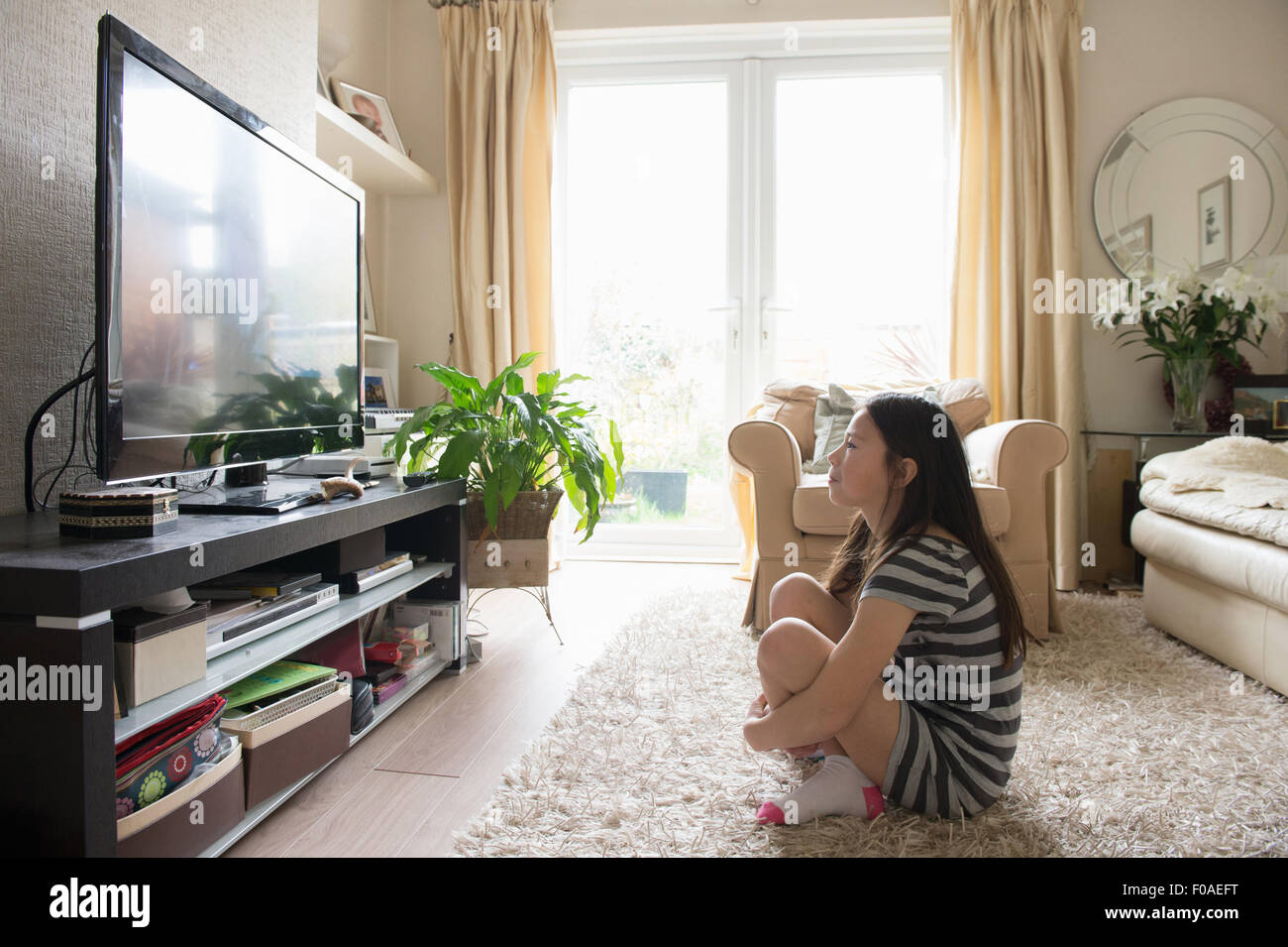 Girl sitting on rug watching the television Stock Photo