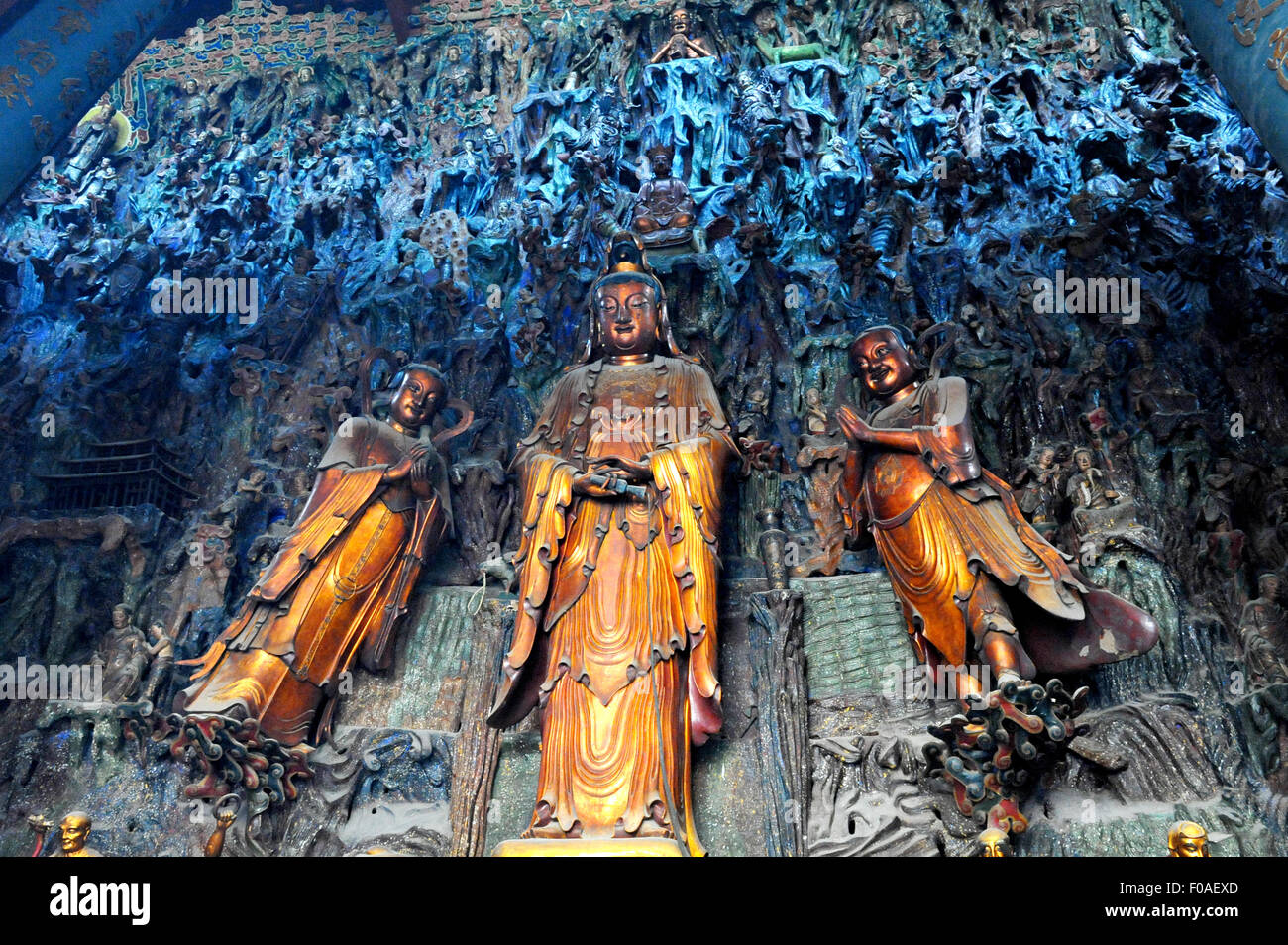 A wall full of Chinese buddha stone statues, including three golden