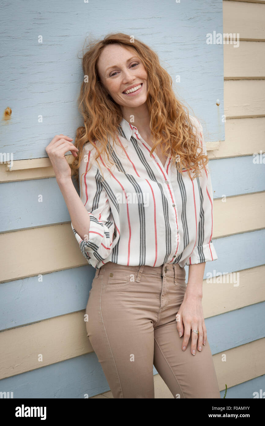 Attractive redhead woman smiling leaning against a beach hut. Stock Photo