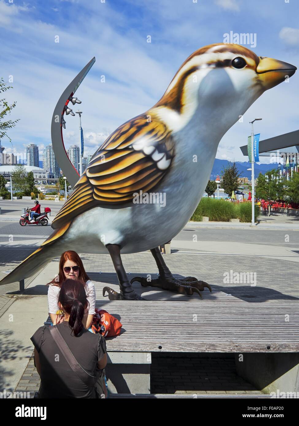 Two women sitting besides giant bird statue in Olympic Village
