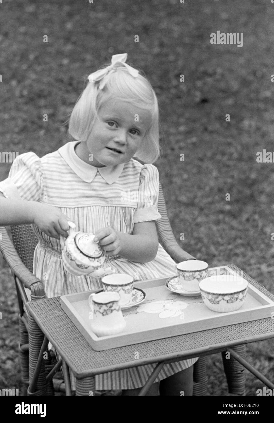 A little girl playing with her table and tea pot set in the garden. Stock Photo