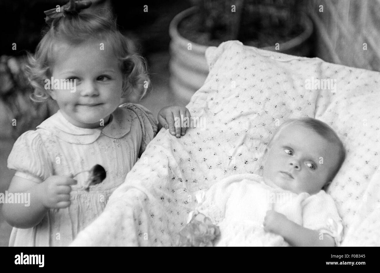 A little girl standing at the side of a bed with a small baby. Stock Photo