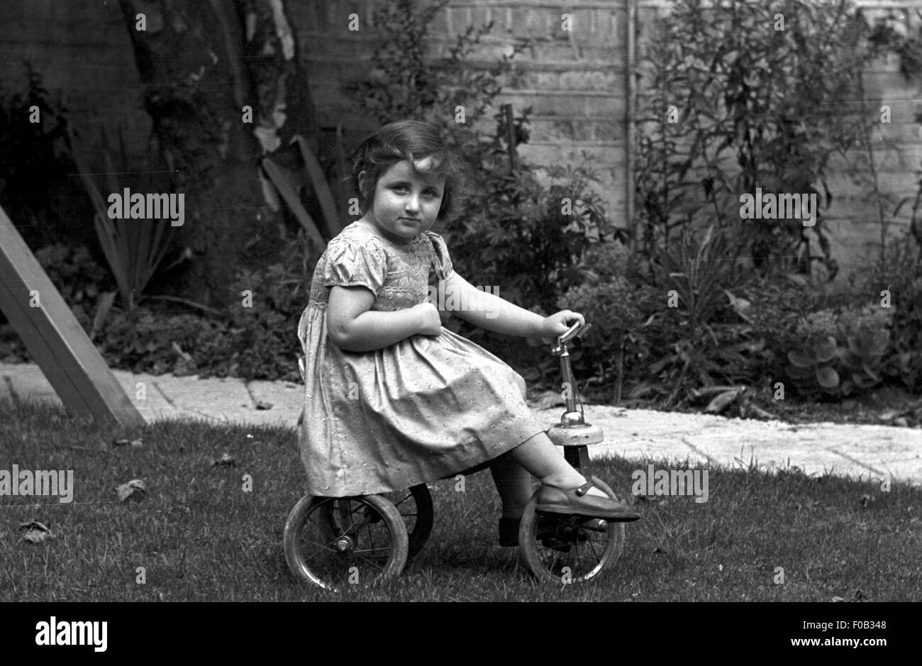 A young girl on her tricycle in the garden Stock Photo