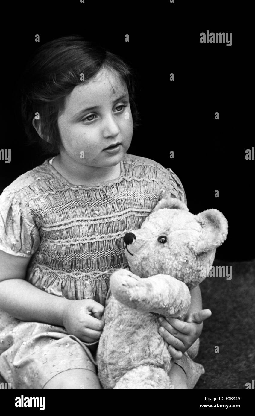 A little girl sitting on a doorstep with her teddy bear Stock Photo