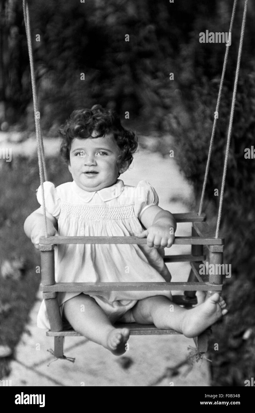 A little girl on a swing in the garden. Stock Photo