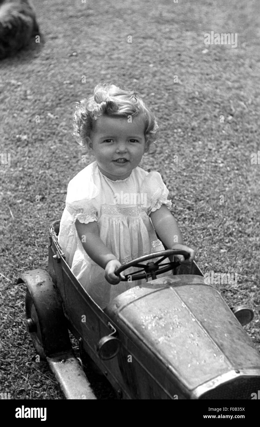 A little girl in a toy tin car smiling. Stock Photo