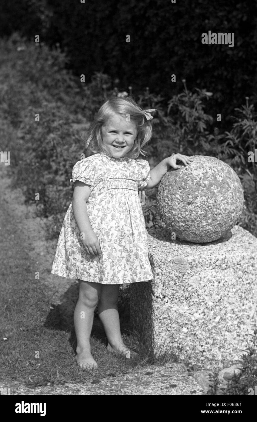 A little girl wearing a summer dress standing next to a stone ball garden feature Stock Photo